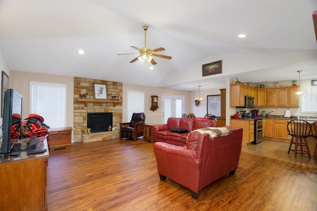 living room with hardwood / wood-style floors, ceiling fan with notable chandelier, a stone fireplace, and lofted ceiling