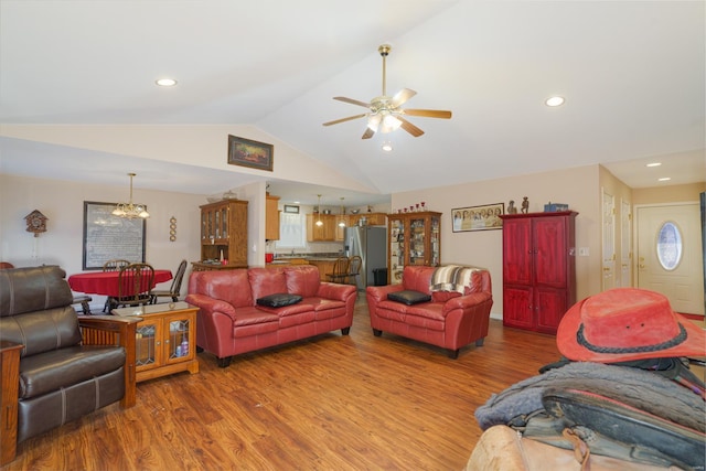 living room featuring ceiling fan with notable chandelier, wood-type flooring, and vaulted ceiling