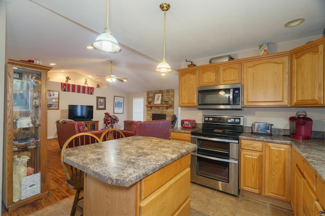 kitchen with appliances with stainless steel finishes, ceiling fan, pendant lighting, a stone fireplace, and lofted ceiling