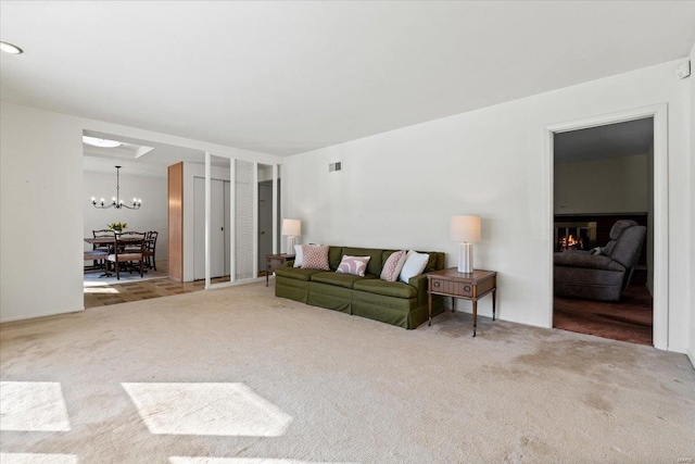 living room with a chandelier, a glass covered fireplace, carpet flooring, and visible vents