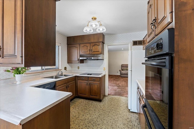 kitchen featuring wallpapered walls, a peninsula, light countertops, black appliances, and a sink