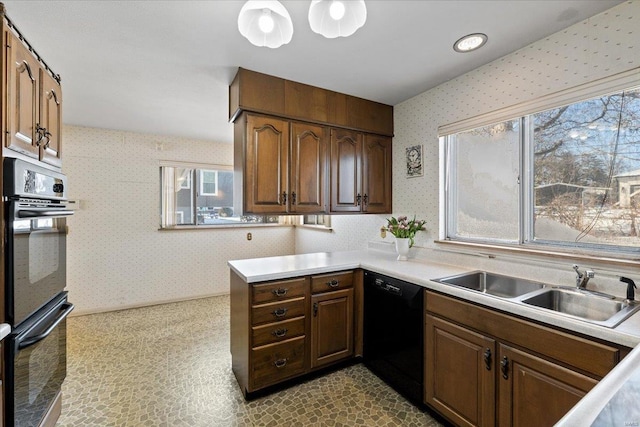 kitchen with wallpapered walls, light countertops, a healthy amount of sunlight, black appliances, and a sink