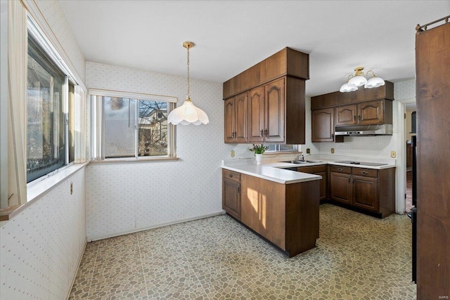 kitchen with wallpapered walls, under cabinet range hood, pendant lighting, and light countertops