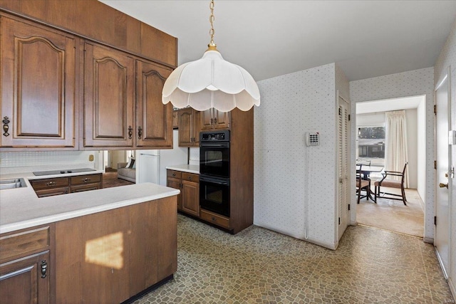 kitchen with dobule oven black, light countertops, hanging light fixtures, a peninsula, and wallpapered walls