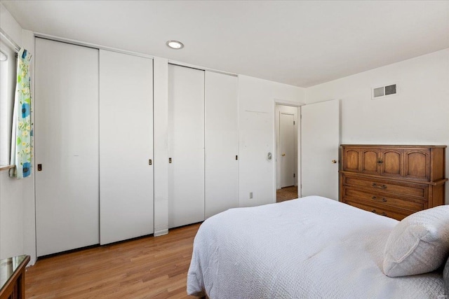 bedroom with visible vents, light wood-style flooring, and two closets