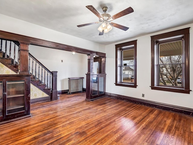 unfurnished living room featuring radiator, ceiling fan, ornate columns, and dark hardwood / wood-style floors