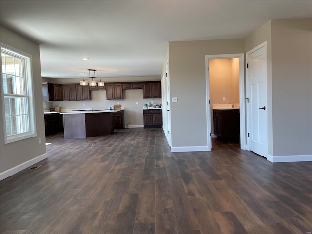 kitchen with dark brown cabinetry, dark wood-type flooring, a chandelier, pendant lighting, and a kitchen island