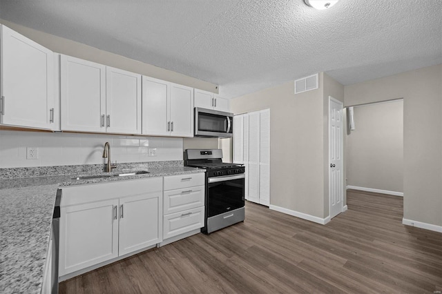 kitchen with appliances with stainless steel finishes, a textured ceiling, sink, dark hardwood / wood-style floors, and white cabinetry