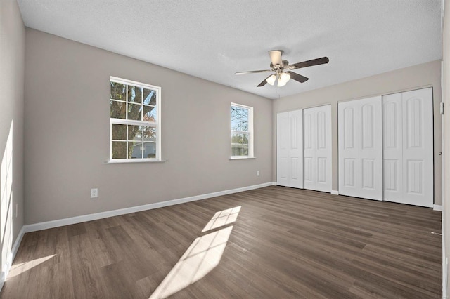 unfurnished bedroom with ceiling fan, dark hardwood / wood-style floors, a textured ceiling, and multiple closets