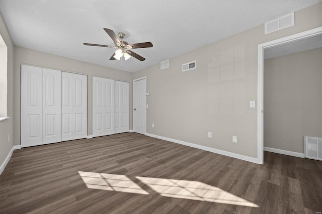 unfurnished bedroom featuring multiple closets, a textured ceiling, ceiling fan, and dark wood-type flooring