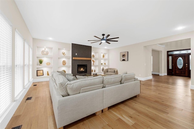 living room featuring a fireplace, built in shelves, light hardwood / wood-style floors, and a healthy amount of sunlight