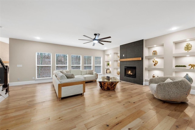 living room with a tile fireplace, light hardwood / wood-style flooring, built in features, and ceiling fan