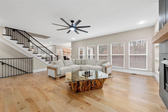 living room with a tile fireplace, ceiling fan, and light hardwood / wood-style floors