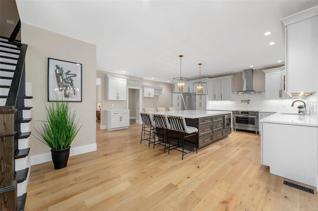 kitchen featuring wall chimney exhaust hood, a kitchen island, decorative light fixtures, a breakfast bar, and stainless steel stove