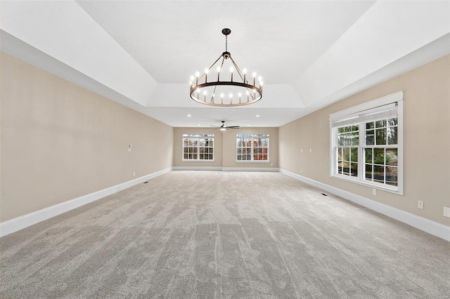 unfurnished living room featuring ceiling fan with notable chandelier, light colored carpet, and a raised ceiling