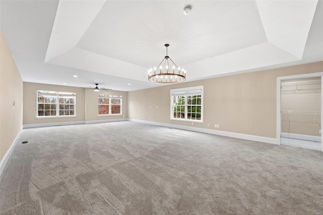 unfurnished living room with carpet flooring, ceiling fan with notable chandelier, and a raised ceiling