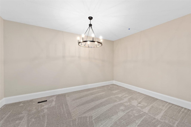 carpeted empty room featuring an inviting chandelier