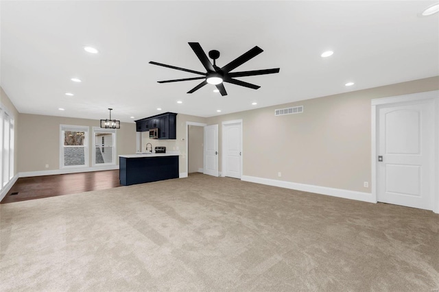 unfurnished living room with dark colored carpet, ceiling fan with notable chandelier, and sink