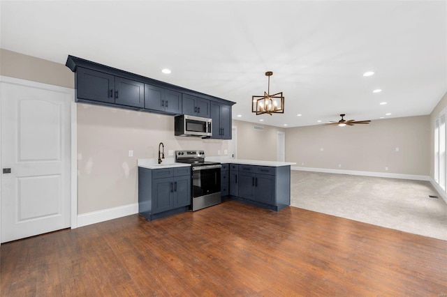 kitchen with dark wood-type flooring, ceiling fan with notable chandelier, appliances with stainless steel finishes, decorative light fixtures, and kitchen peninsula