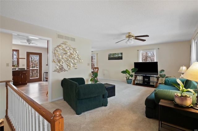 living room featuring light carpet, a textured ceiling, and ceiling fan