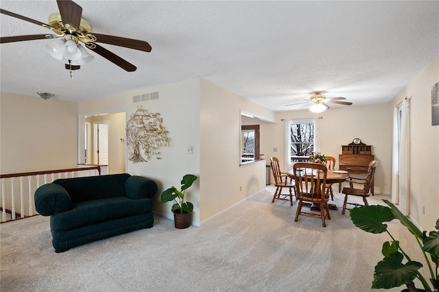 dining space featuring light carpet, ceiling fan, and a textured ceiling