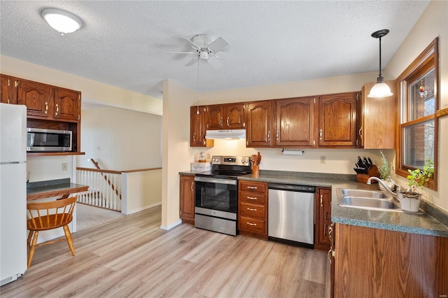 kitchen with a textured ceiling, stainless steel appliances, sink, pendant lighting, and light hardwood / wood-style flooring