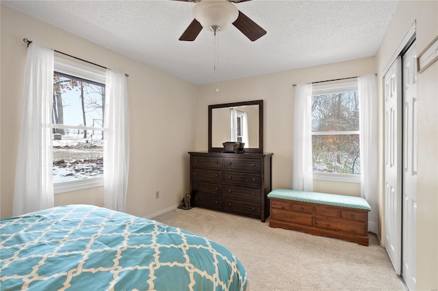 bedroom featuring a textured ceiling, ceiling fan, light carpet, and multiple windows