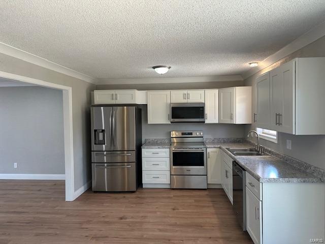 kitchen with appliances with stainless steel finishes, crown molding, sink, white cabinets, and dark hardwood / wood-style floors