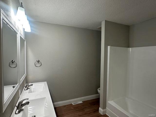 bathroom with hardwood / wood-style floors, a textured ceiling, walk in shower, and sink