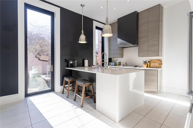 kitchen featuring wall chimney exhaust hood, kitchen peninsula, pendant lighting, a breakfast bar, and light tile patterned floors