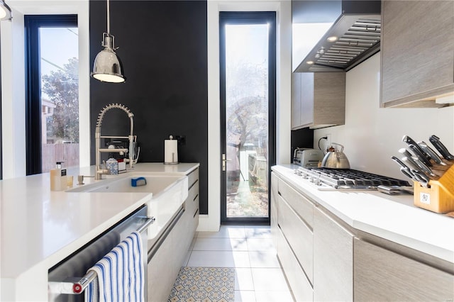 kitchen featuring wall chimney exhaust hood, stainless steel gas cooktop, sink, light tile patterned floors, and decorative light fixtures