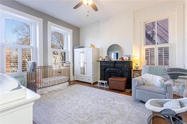 bedroom with ceiling fan, wood-type flooring, and a nursery area