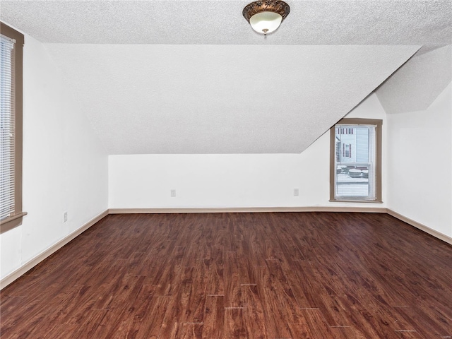 bonus room with a textured ceiling, plenty of natural light, lofted ceiling, and dark wood-type flooring