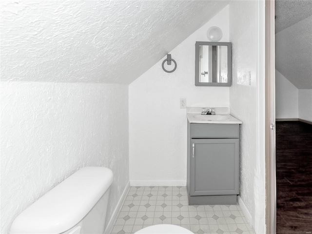 bathroom featuring a textured ceiling, vanity, lofted ceiling, and toilet