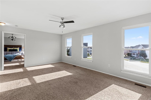 carpeted empty room with ceiling fan with notable chandelier and a healthy amount of sunlight