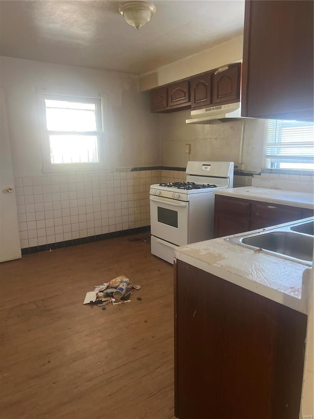 kitchen with dark hardwood / wood-style flooring, dark brown cabinets, white range with gas cooktop, sink, and tile walls