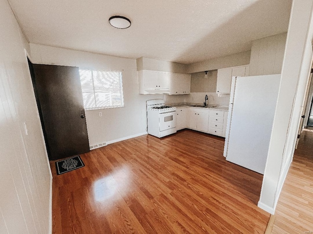 kitchen with white cabinetry, sink, light hardwood / wood-style floors, and white appliances