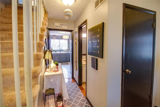 hallway with sink, a textured ceiling, and hardwood / wood-style flooring