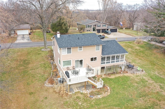 back of property featuring a yard, a garage, a deck, and a sunroom