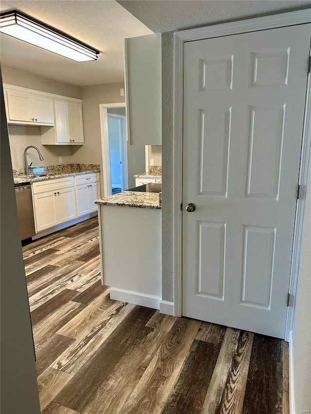 kitchen with sink, dishwasher, white cabinetry, dark hardwood / wood-style floors, and light stone counters