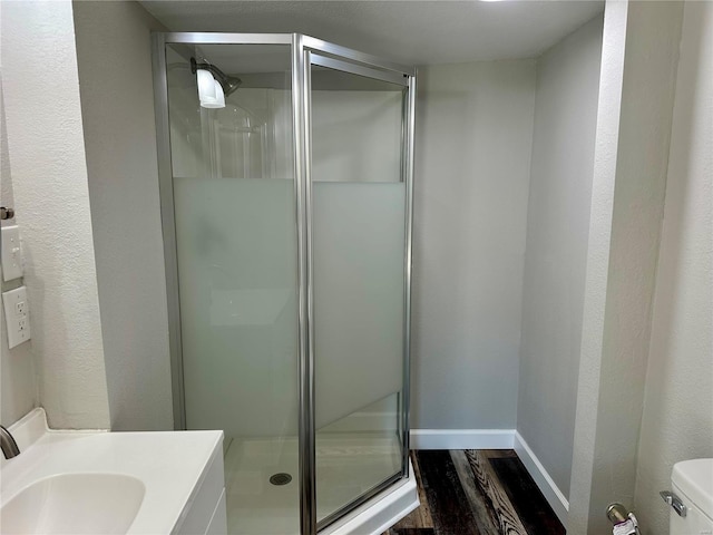 bathroom with hardwood / wood-style flooring, vanity, a shower with shower door, and toilet