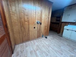 clothes washing area featuring cabinets, light wood-type flooring, and wood walls