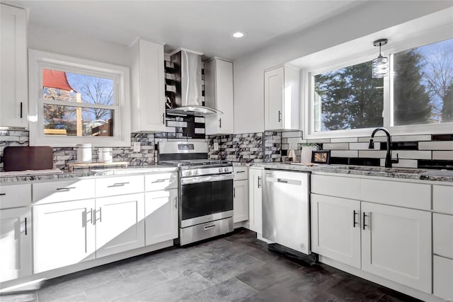 kitchen with white cabinets, appliances with stainless steel finishes, a healthy amount of sunlight, and wall chimney range hood