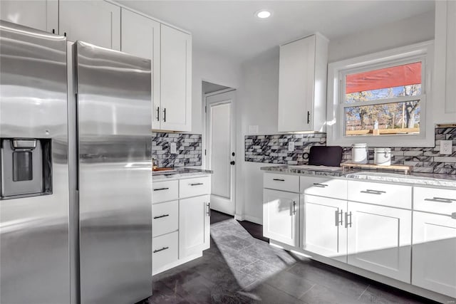 kitchen featuring light stone countertops, stainless steel fridge with ice dispenser, backsplash, white cabinets, and dark tile patterned flooring