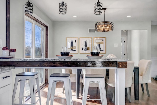 kitchen featuring a kitchen bar, white cabinets, hanging light fixtures, and light hardwood / wood-style floors