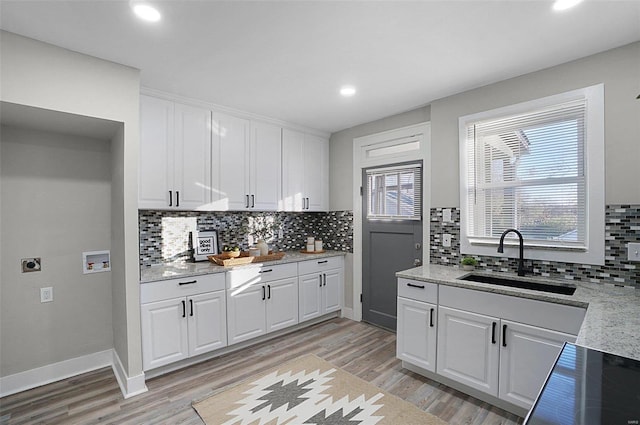 kitchen with white cabinets, sink, light wood-type flooring, tasteful backsplash, and light stone counters