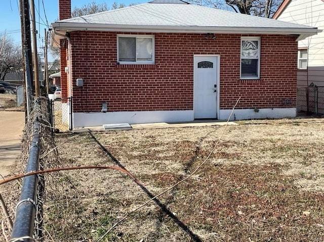 rear view of property featuring brick siding, a chimney, and fence