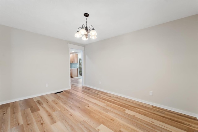 spare room with light wood-type flooring and a notable chandelier