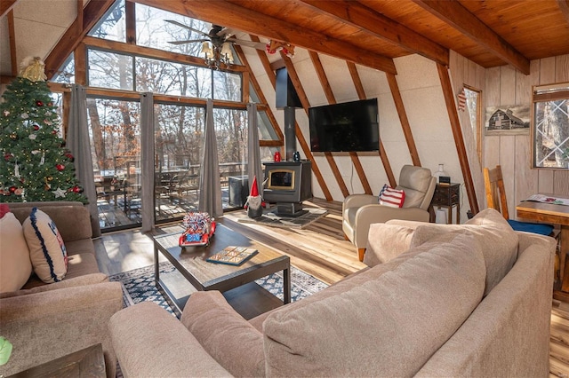 living room featuring hardwood / wood-style floors, a wood stove, wooden walls, ceiling fan, and beam ceiling