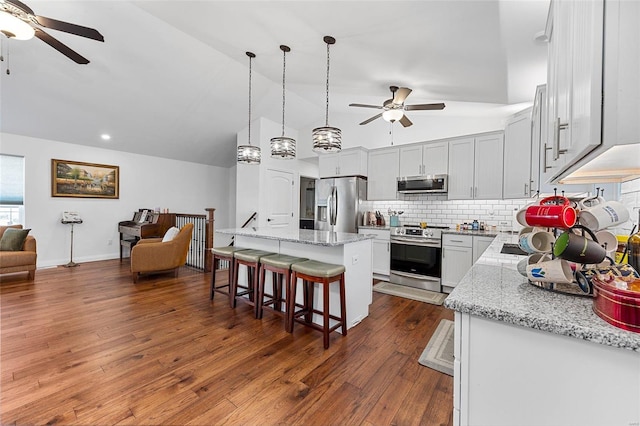 kitchen with dark hardwood / wood-style flooring, light stone countertops, a center island, and appliances with stainless steel finishes